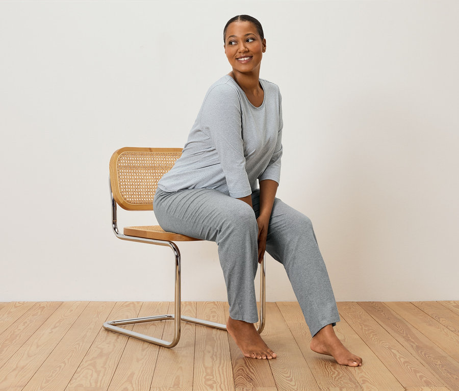 Nő ül egy széken szürke csíkos pizsamában.