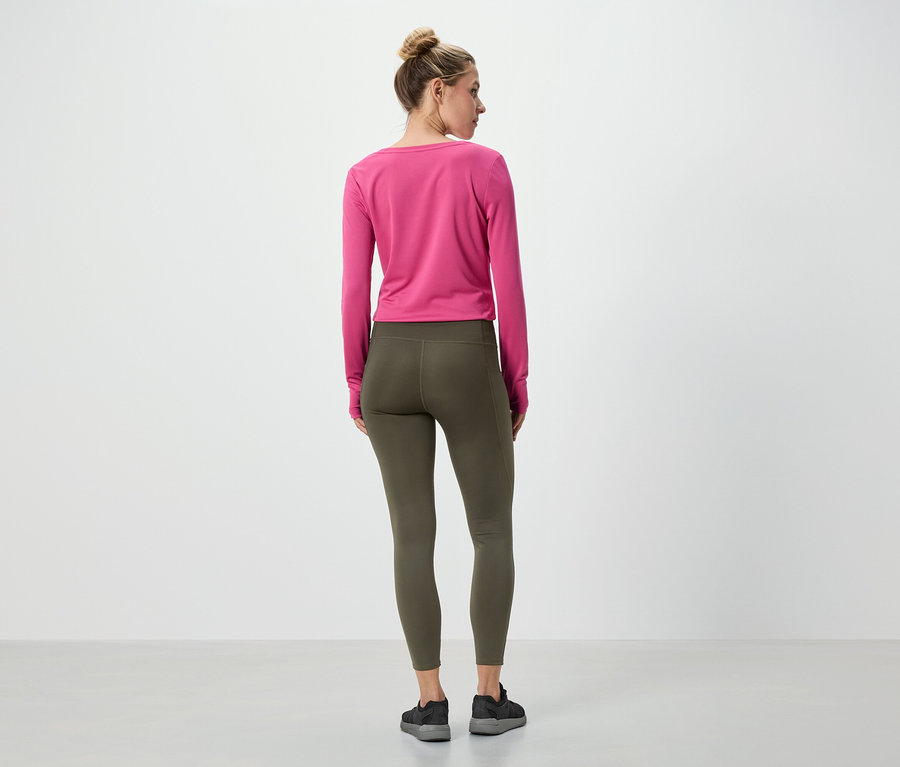 Egy nő áll háttal a kamerának, rózsaszín hosszú ujjú felsőt és olívazöld leggingset visel.