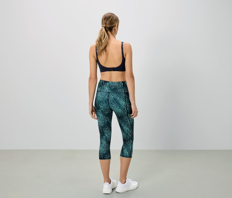 Hátulról látható nő sportmelltartót és mintás zöld Capri leggingset visel.