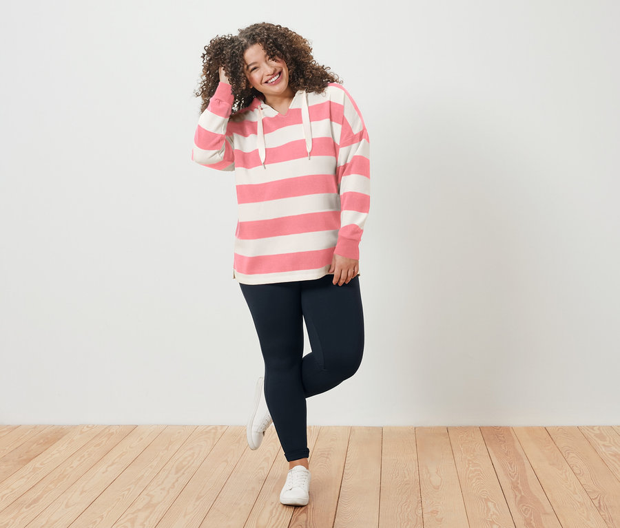 Mosolygó, göndör hajú nő csíkos kapucnis pulóverben és leggingsben.