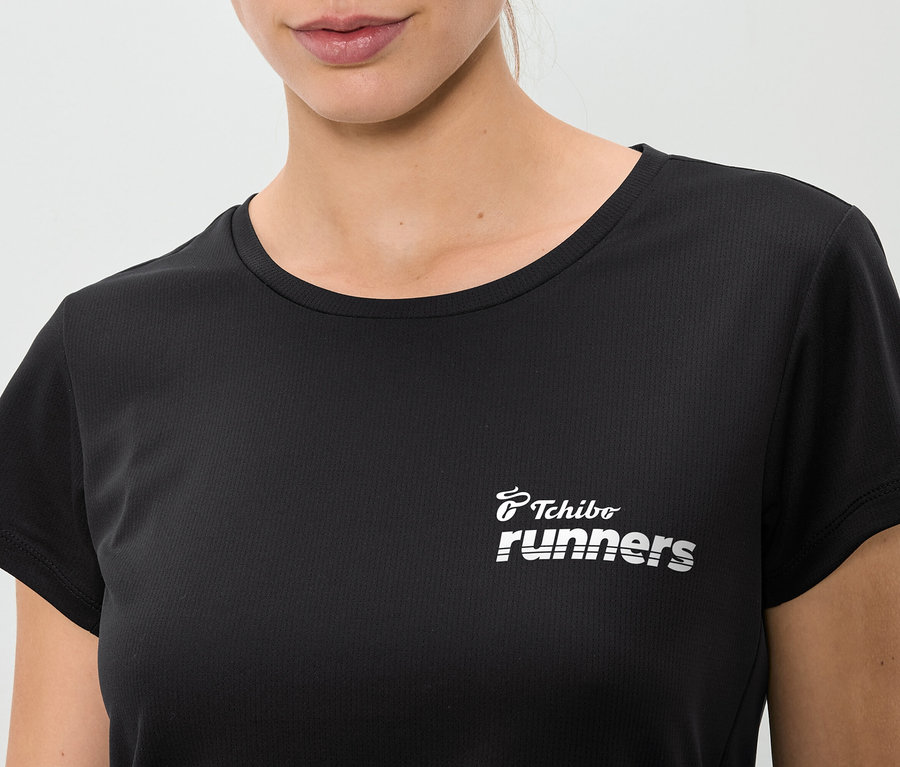 Közeli kép egy fekete, "Tchibo runners" feliratú pólót viselő nőről.