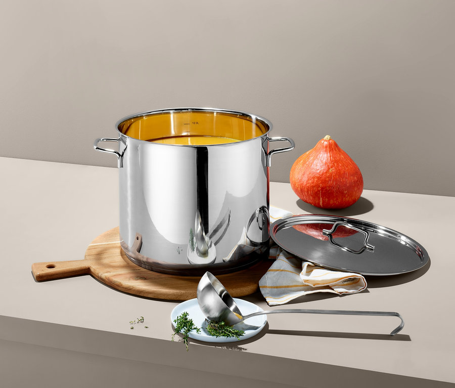 Egy XL-es nemesacél leveses fazék áll egy fa vágódeszkán egy tök mellett. Egy fedő és egy merőkanál a fazék mellett fekszik.