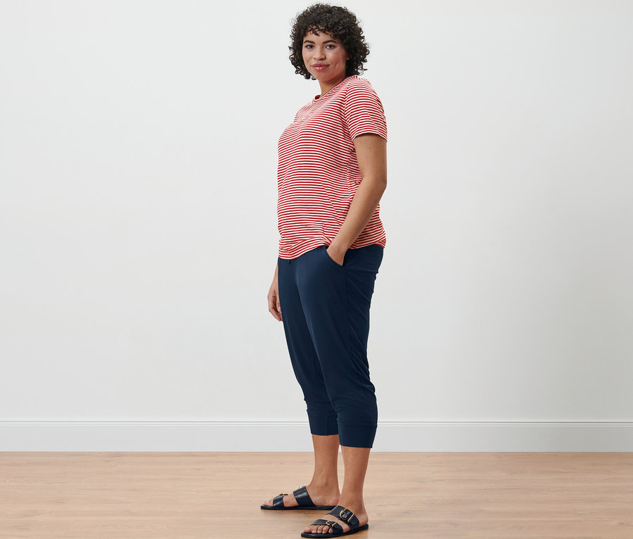 Nő csíkos felsőben és 3/4-es jersey nadrágban áll oldalra fordulva.