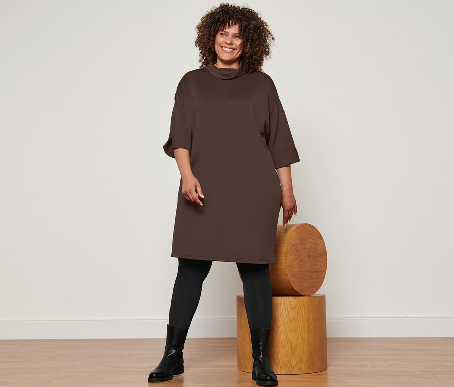 Nő pózol Női 3/4-es ujjú lezser ruhában, sötétbarna, Női termo harisnyanadrágban, fekete és Női bőrcsizmában, fekete.