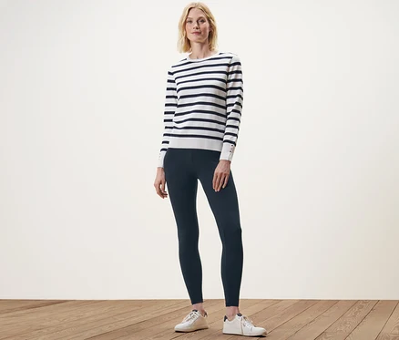 Nő áll sötétkék leggingsben és egy csíkos pulóverben.