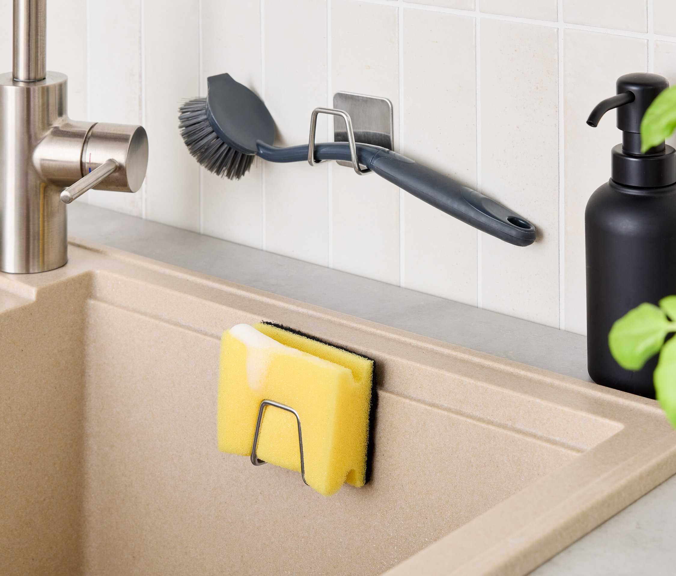 A konyhában egy bézs mosogató található csapteleppel. A falon egy tartó kefével, a mosogatón pedig egy tartó szivaccsal. A mosogató mellett egy fekete üveg áll.