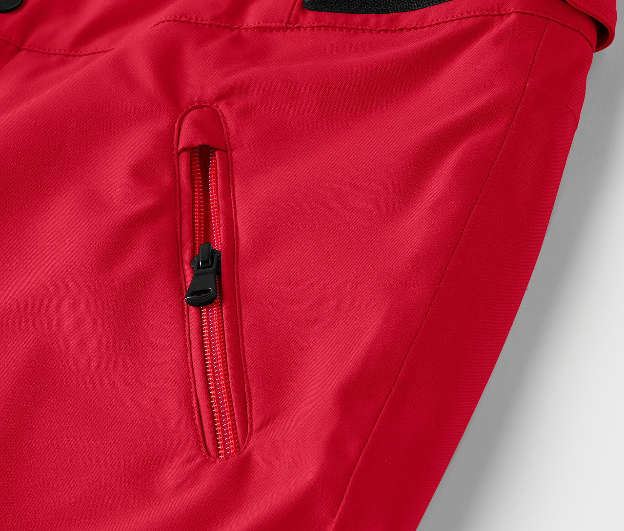 Egy piros kabát részlete fekete cipzárral a zseben.