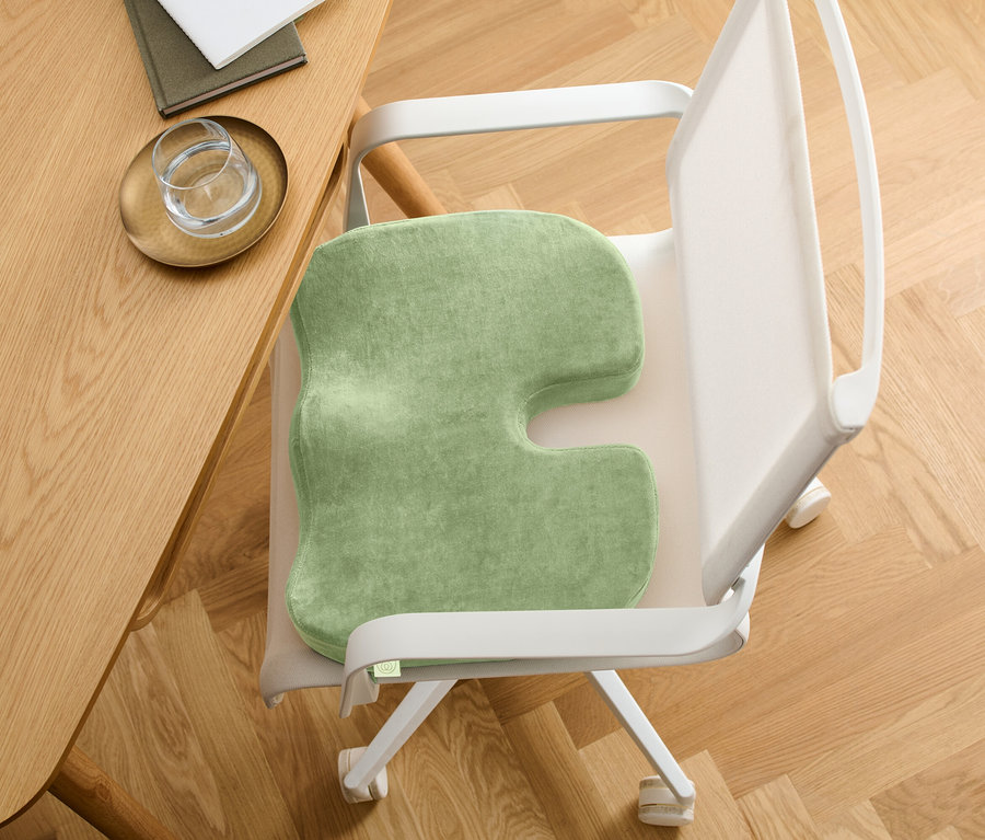 Zöld ülőpárna U alakú kivágással egy széken. A szék egy fa asztal mellett áll.