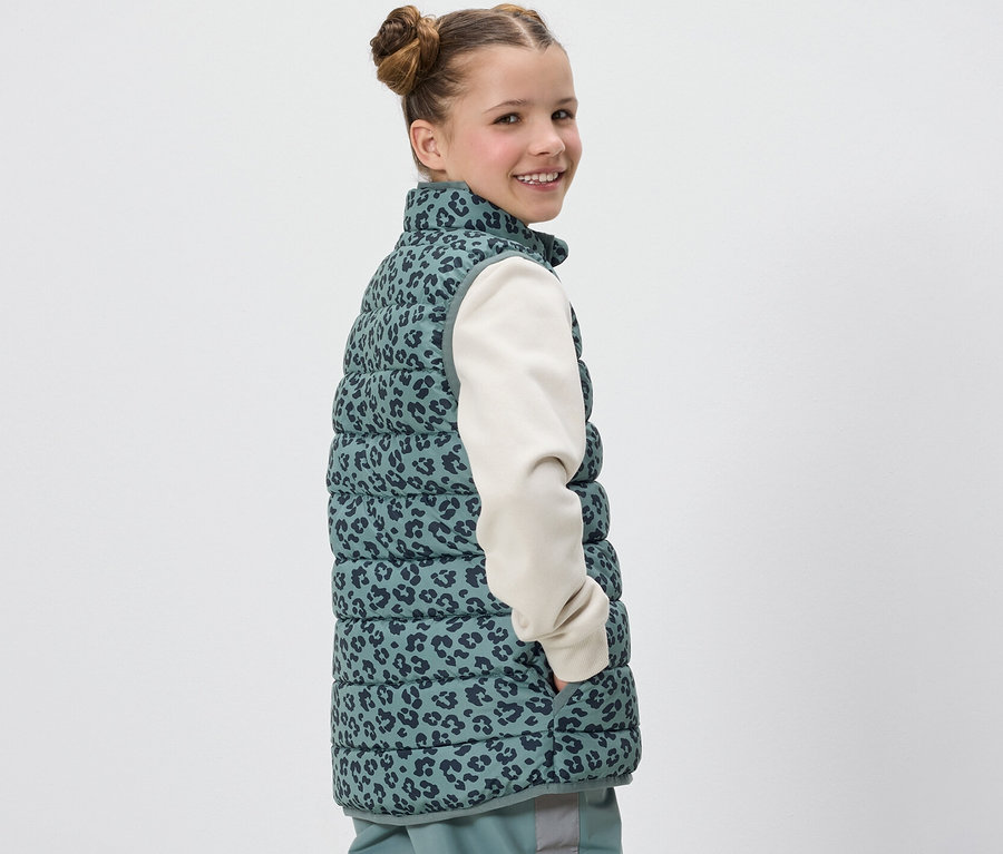 A lány a válla fölött mosolyog, és leopárdmintás Kinder steppelt mellényt visel.