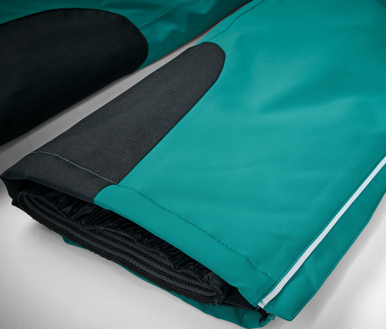 Közeli kép egy smaragdzöld síelőről fekete részletekkel és egy fehér csíkkal.