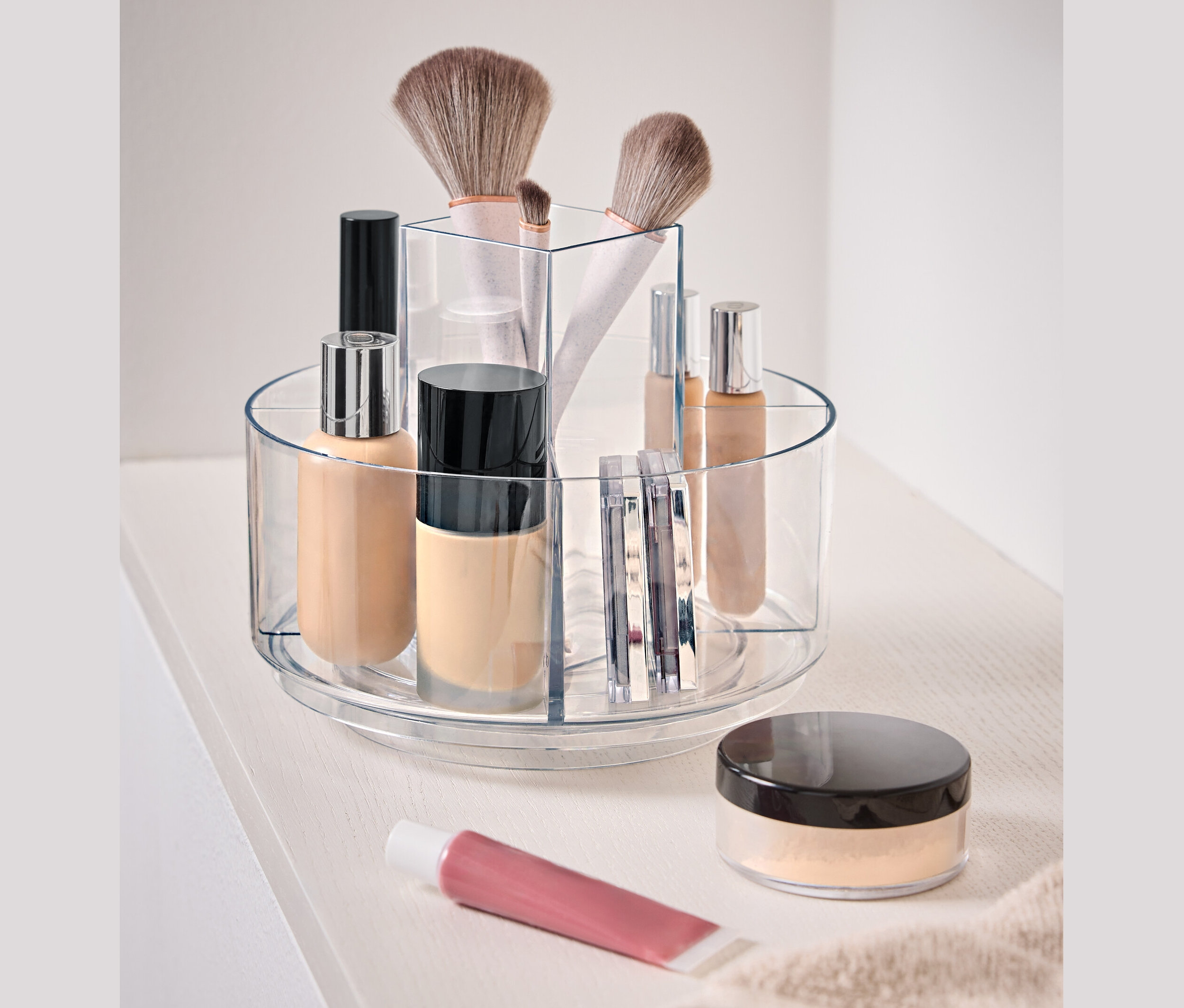 Átlátszó, forgatható tartály kozmetikumokkal fehér felületen.