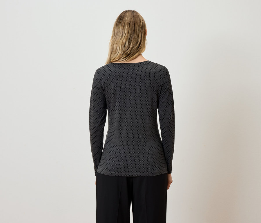 Egy nő háttal a kamerának szürke-fekete, hosszú ujjú blúzt és fekete nadrágot visel.