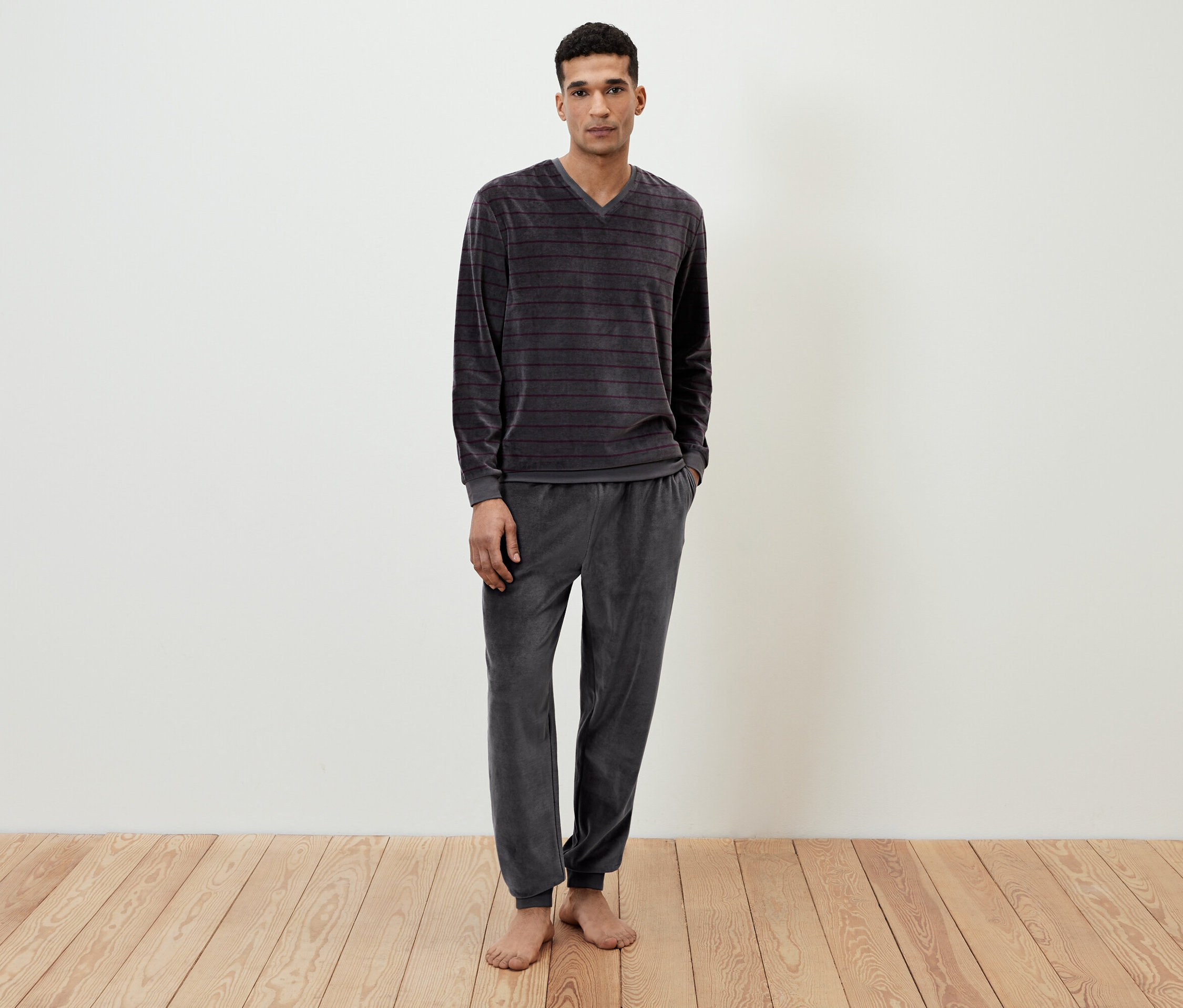 Egy férfi áll mezítláb, szürke, csíkos velúr pizsamában.