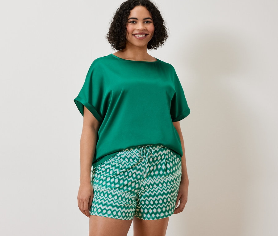 Nő visel egy vízkék, többféle anyagból készült blúzt és 2 jersey rövidnadrágot.