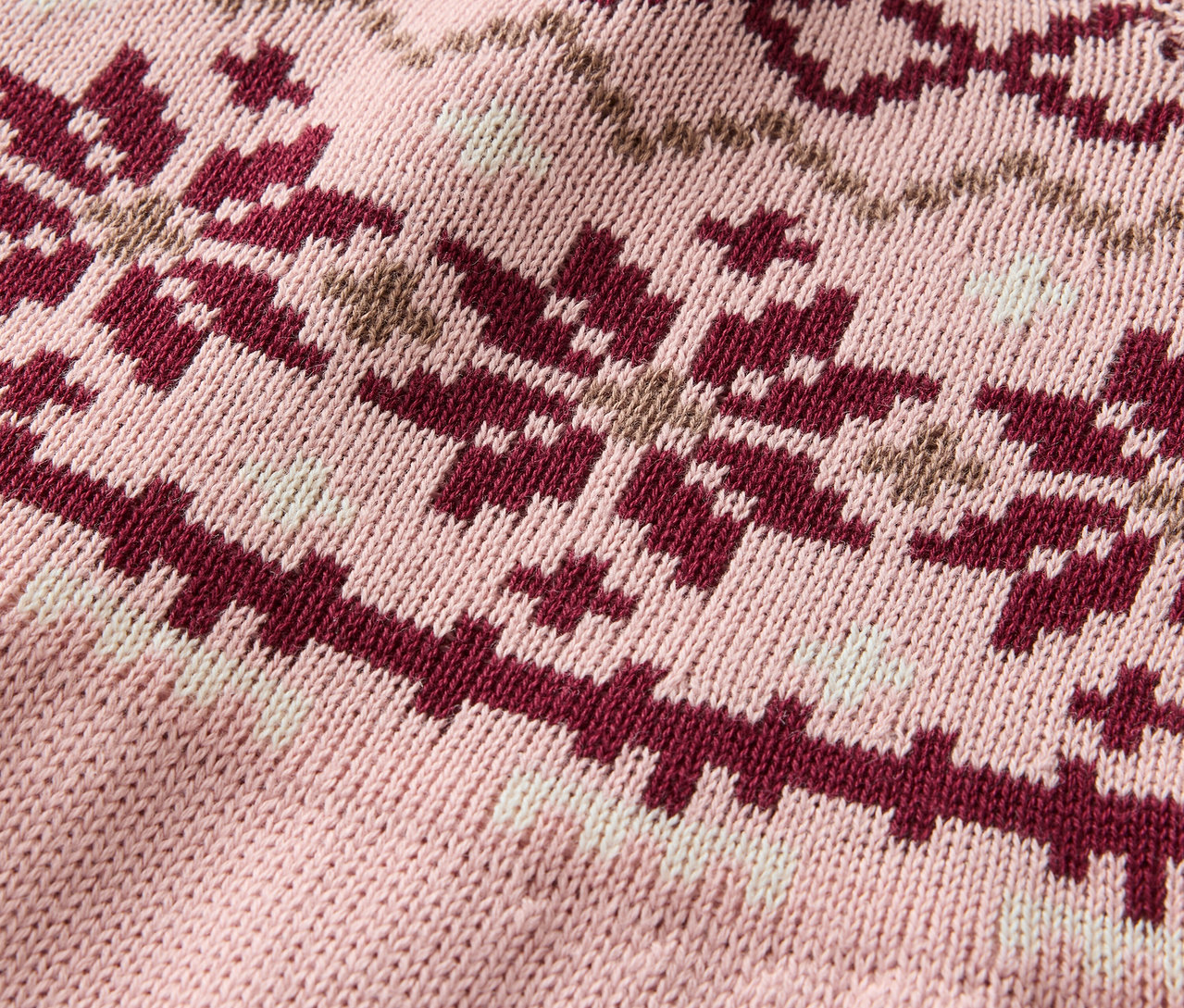 Egy rózsaszín kötött pulóver részlete bordó és bézs hópelyhek mintázatával.