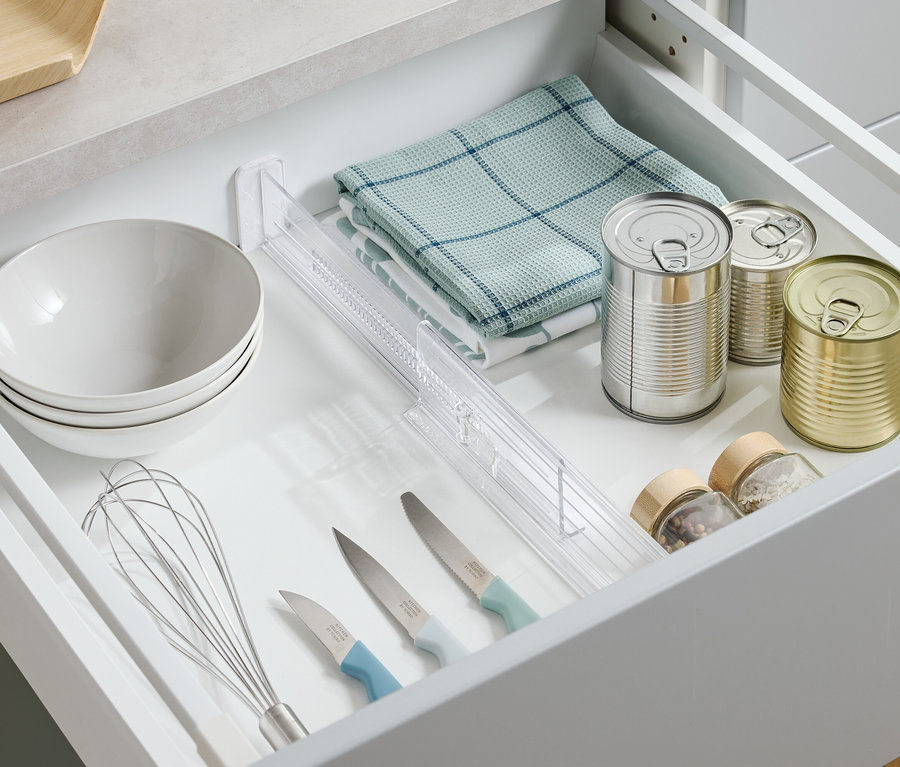 Felülnézet egy nyitott fiókra, amelyben tálak, konyharuha, konzervdobozok, fűszerek, kések és habverő található.