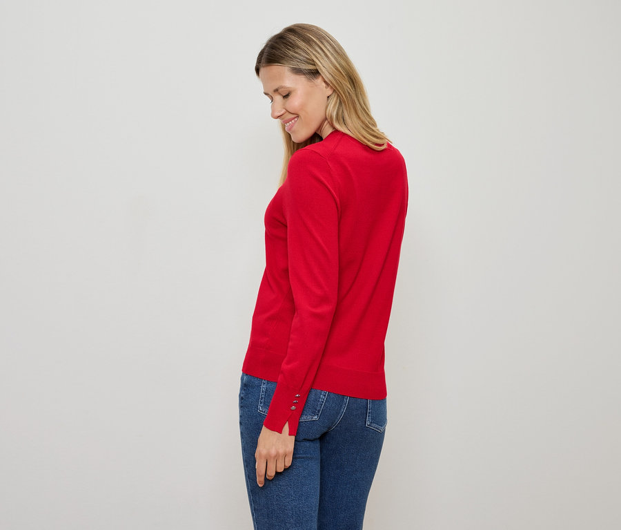 Nő piros pulóverben és kék farmerben, lefelé nézve.