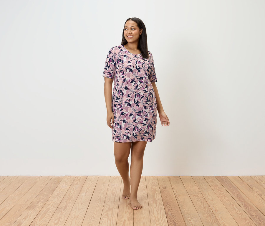 Egy nő mezítláb sétál a fapadlón, virágos ruhát visel.