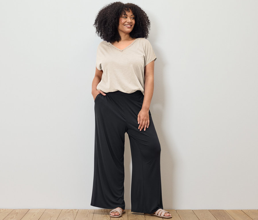 Nő pózol krémfehér modálkeverék pólóban és fekete palazzo nadrágban.