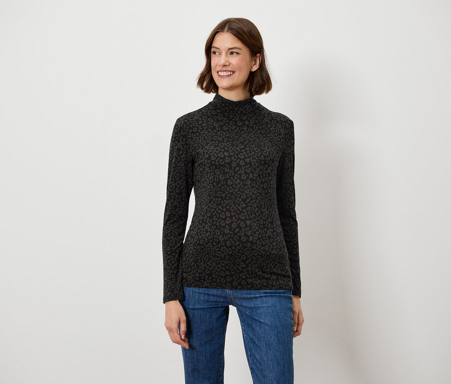 Barna hajú nő mosolyogva pózol fekete, hosszú ujjú felsőben és kék farmerben.