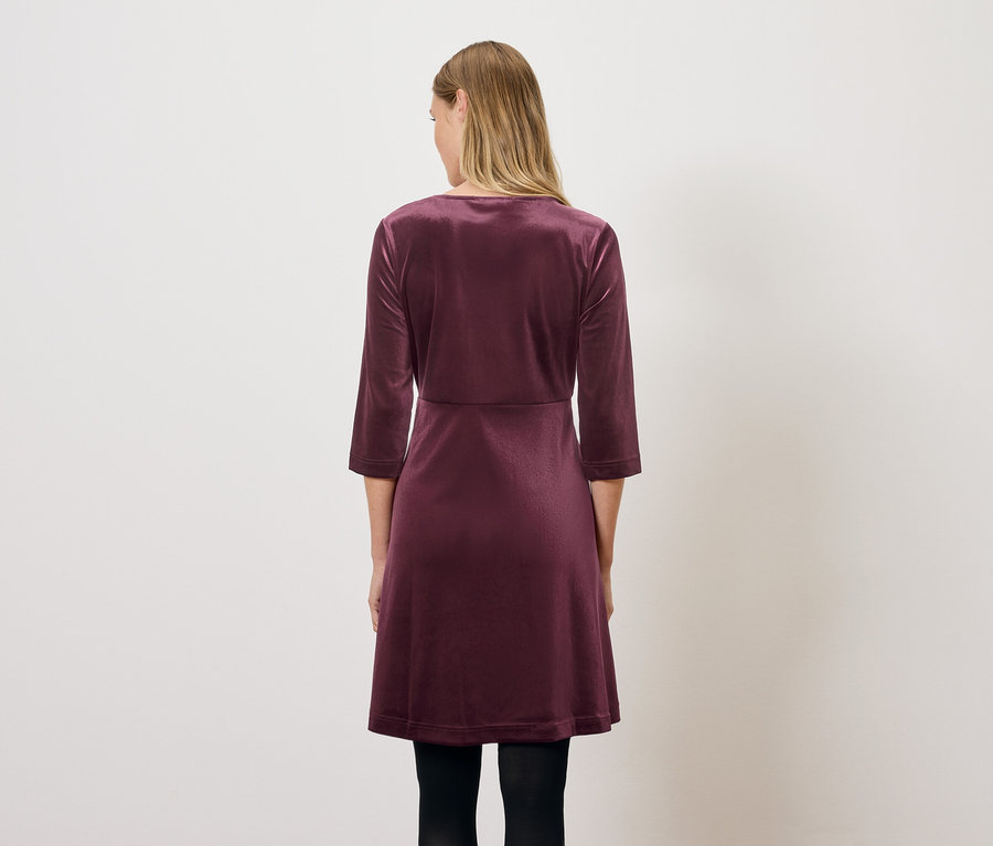 Egy nő háttal áll, és egy bordó, háromnegyedes ujjú bársonyruhát visel.