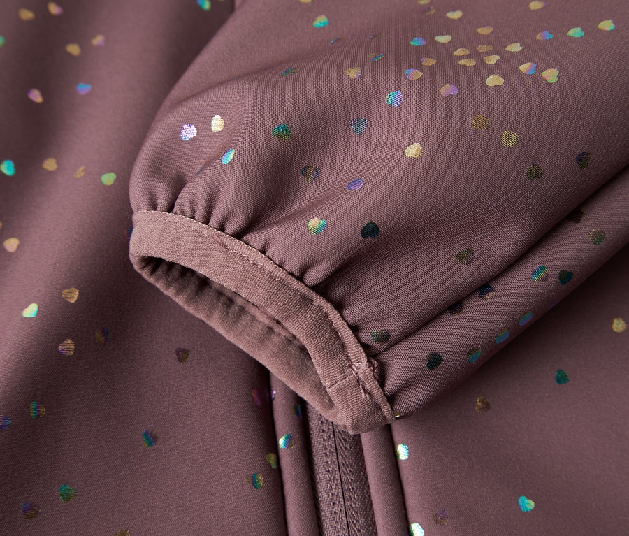 Egy lila softshell kabát ujjának és cipzárjának közeli felvétele, színes szívecskékkel.