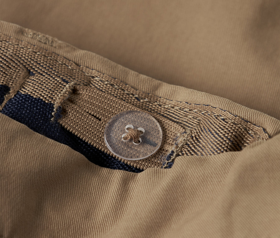 Egy bézs ing közeli képe gombbal és dekoratív szalaggal.