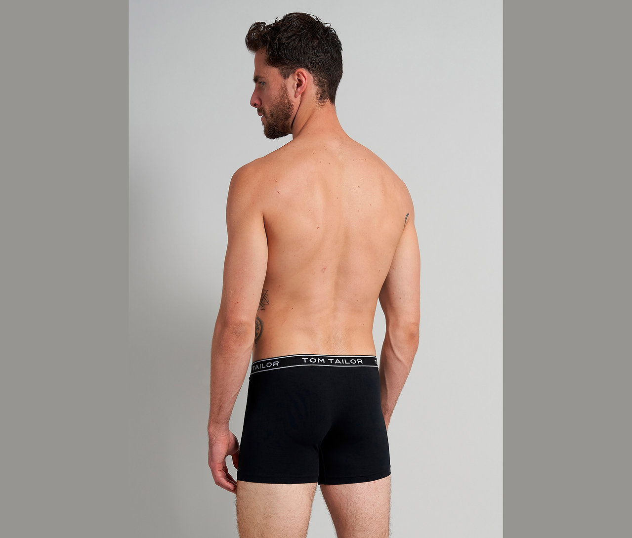 Hátulról látható tetovált férfi fekete Tom Tailor boxeralsóban.