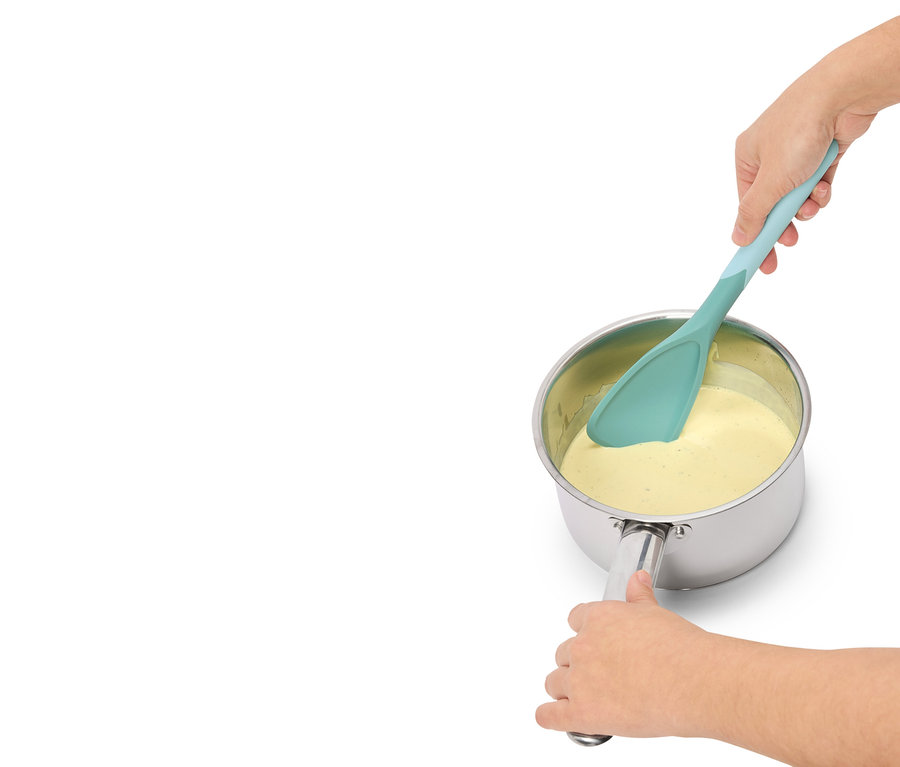 Egy személy türkiz spatulával sárga folyadékot kever egy edényben.
