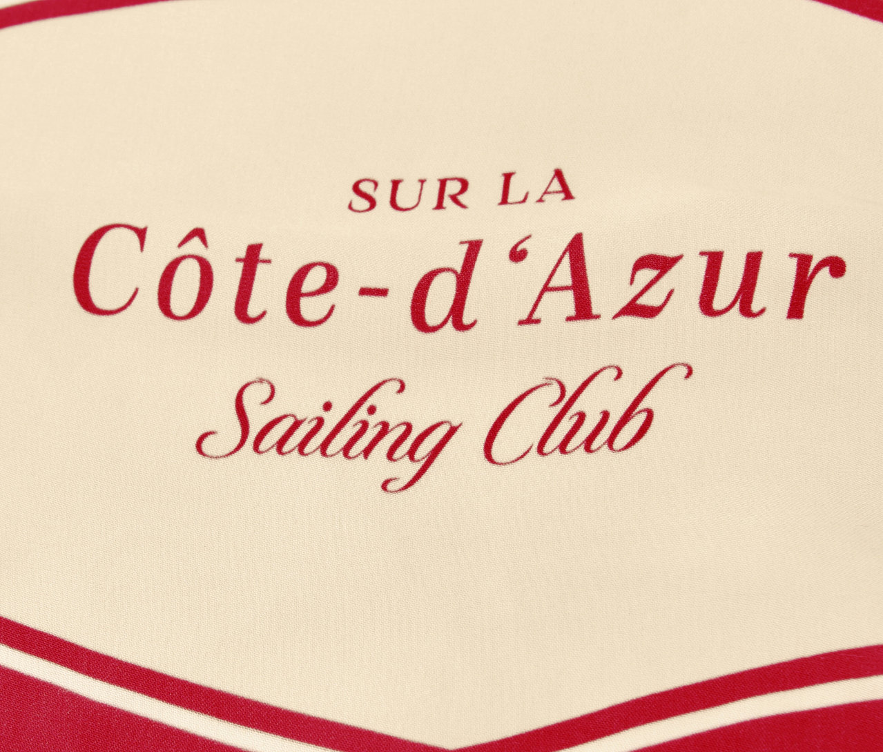 Közelkép a Street One »Nicki« sálról, piros „Côte-d'Azur Sailing Club” felirattal, bézs alapon.