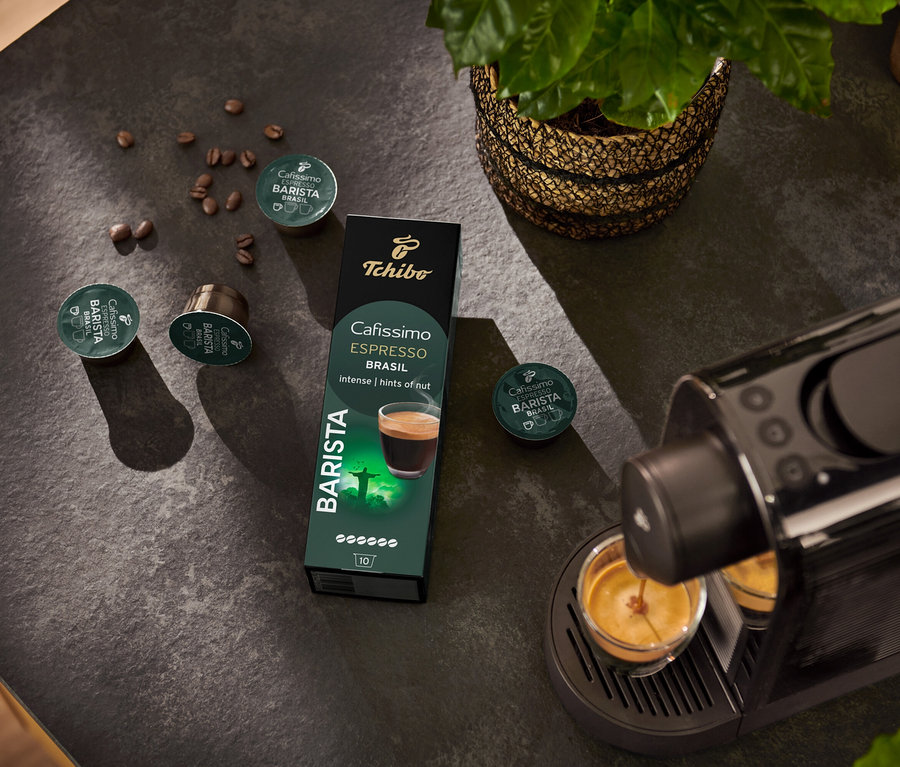 Eszpresszógép tölti a csészét. A háttérben Espresso Brasil - 10 db kávékapszula csomag és kávébab.