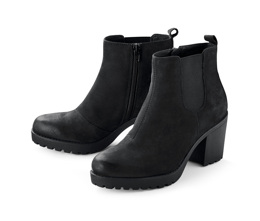 Két fekete, magas sarkú női bőr bokacsizma, az egyik cipzáros.