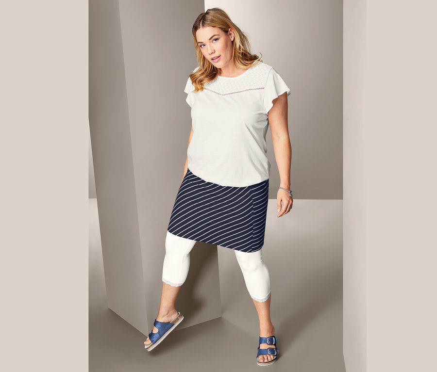 Nő pózol lyukhímzéses felsőben, csíkos dzsörzészoknyában és 3/4-es csipkés leggingsben.