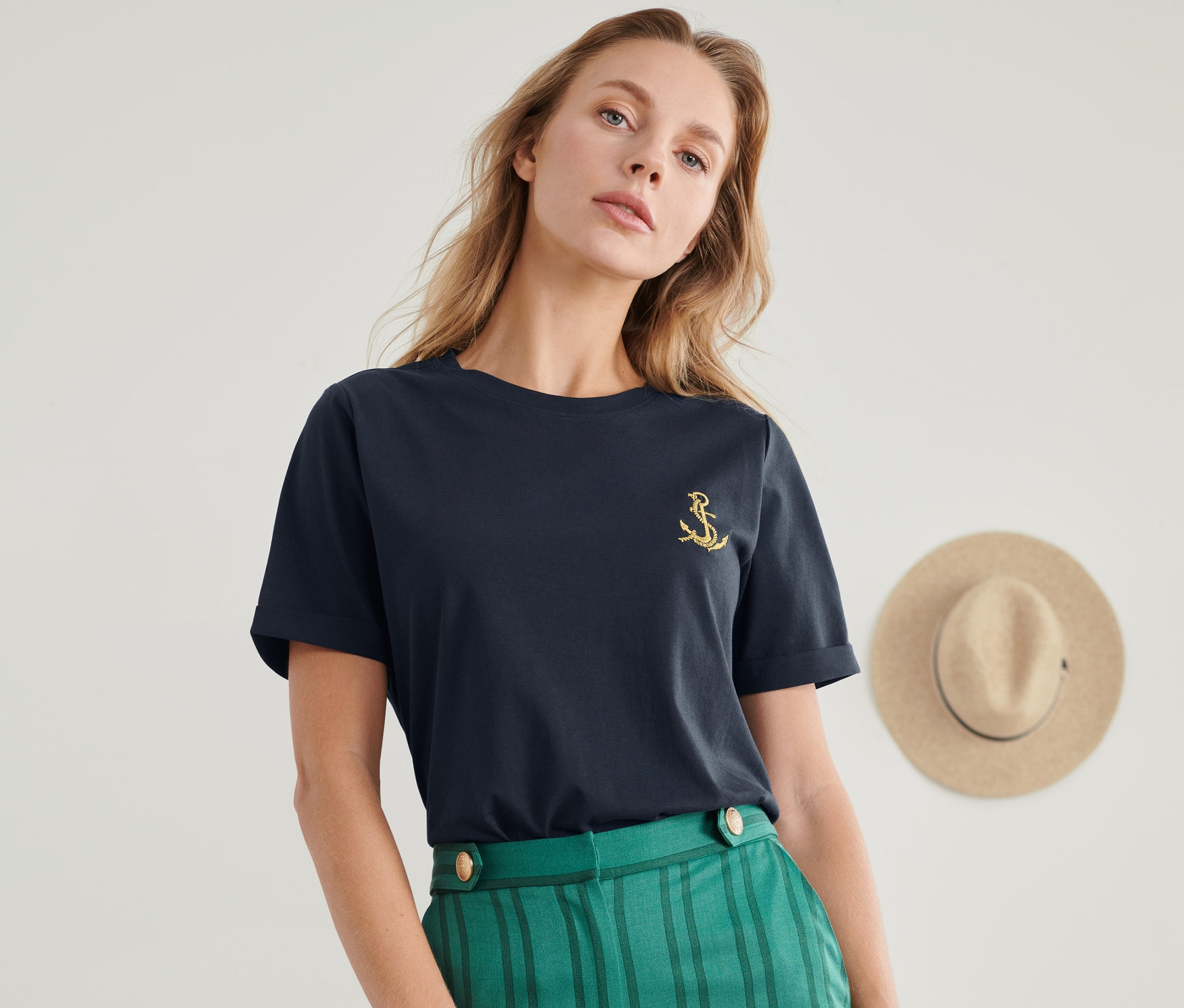 Nő visel horgony hímzéssel ellátott pólót és zöld csíkos nadrágot.