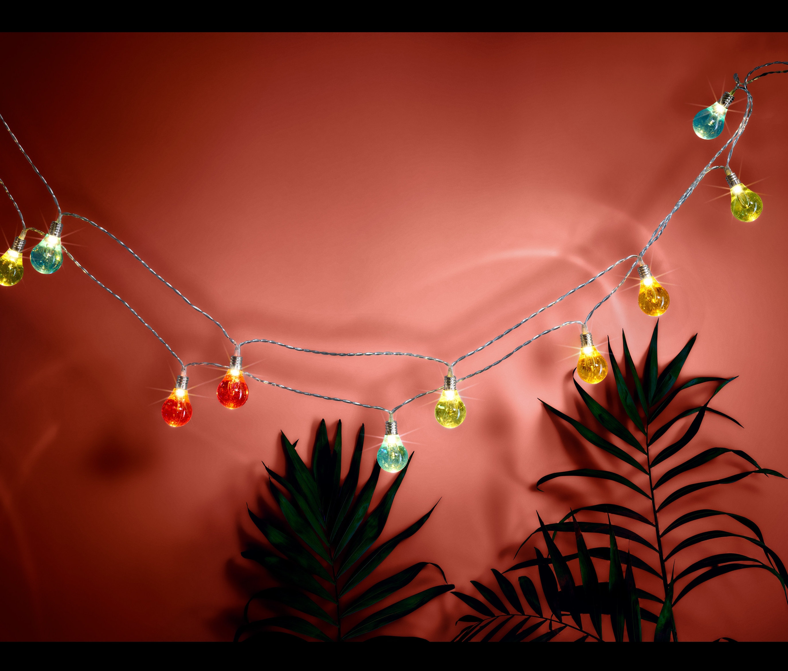 LED-es fényfüzér színes izzókkal, növényekkel a háttérben.