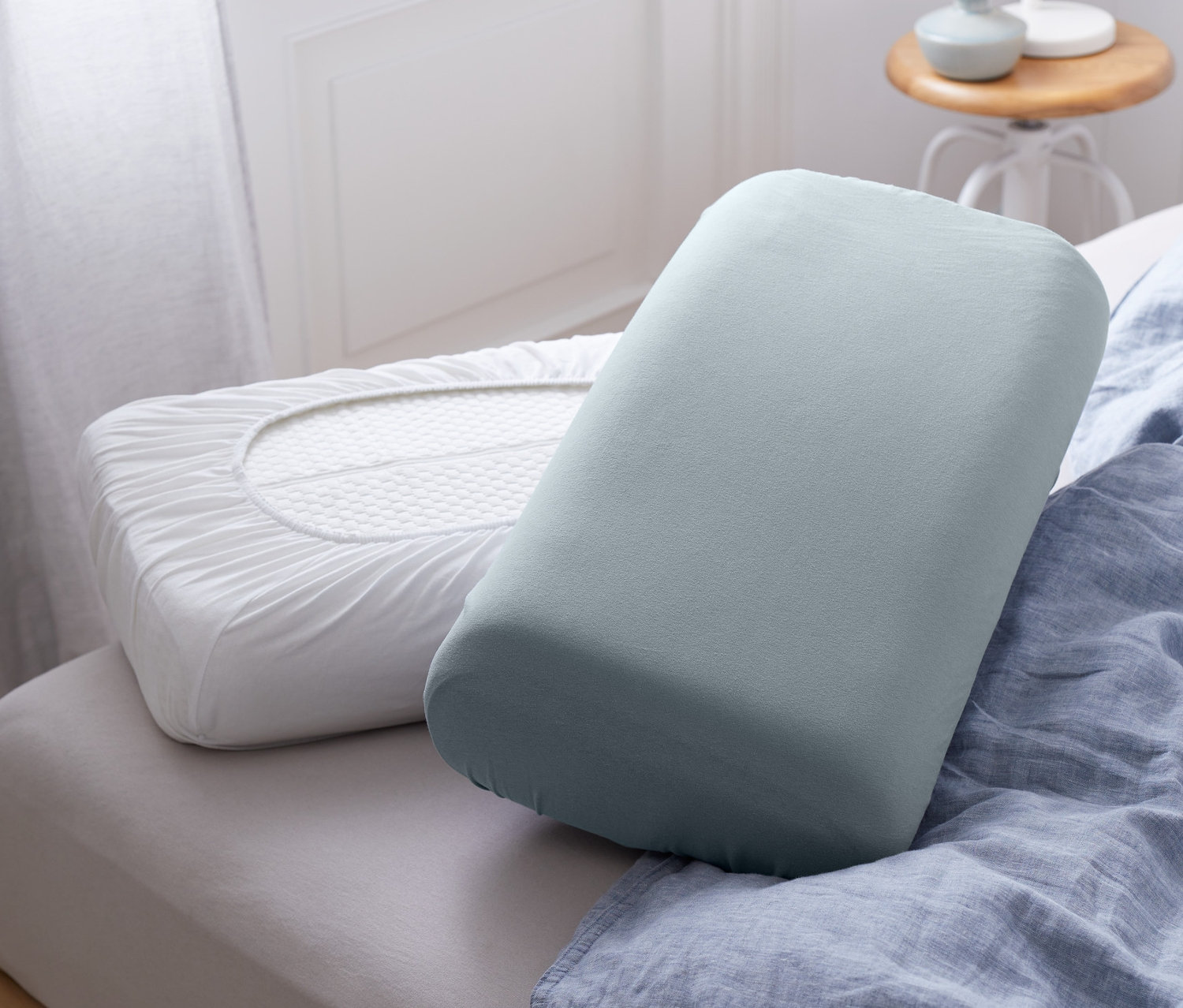 Két gumis párnahuzat fekszik egy ágyon, kék ágyneművel.