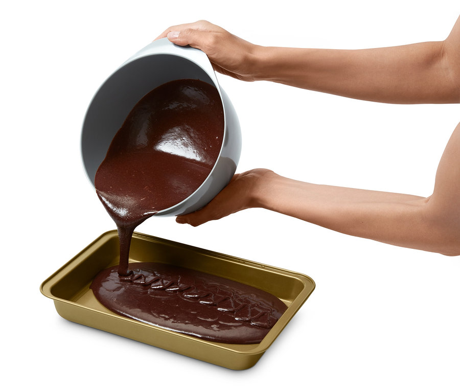 Barna tészta ömlik egy tálból egy brownie sütőformába.