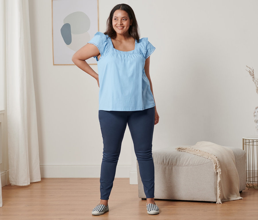 Nő pózol világoskék hímzett trikóban, jeggingsben és espadrillesben.