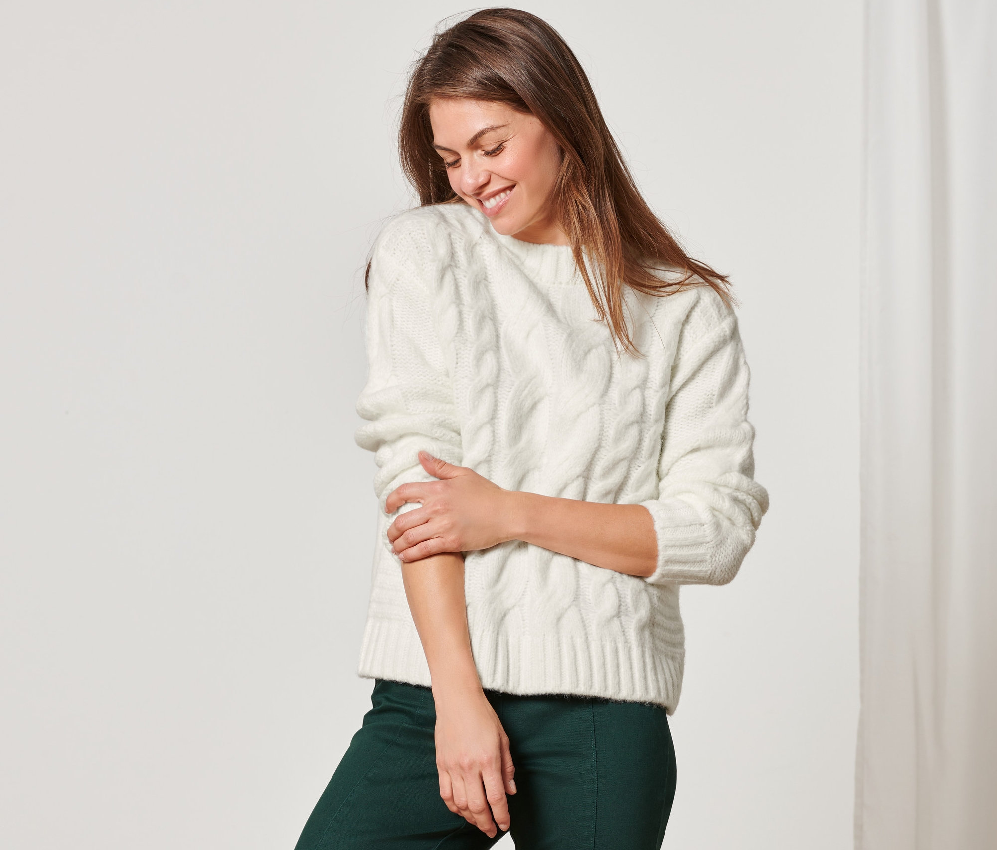 Nő zöld nadrágban és krémszínű kötött pulóverben.