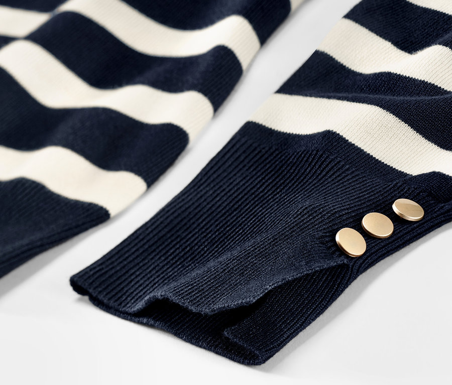 Egy sötétkék, csíkos, finomkötésű női pulóver részlete, gombokkal az ujján.