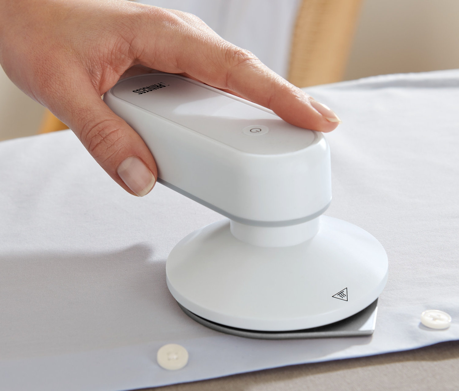 Egy kéz egy fehér inget vasal egy Úti vasaló külső akkumulátorral.