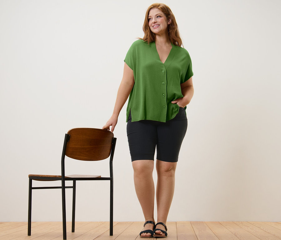 Nő pózol zöld, rövid ujjú kardigánban és fekete bengalin bermudanadrágban.