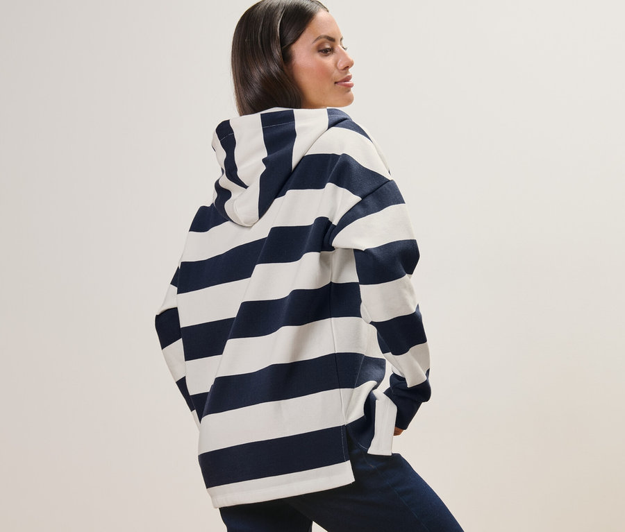 Csíkos kapucnis szabadidőfelsőben pózoló nő.