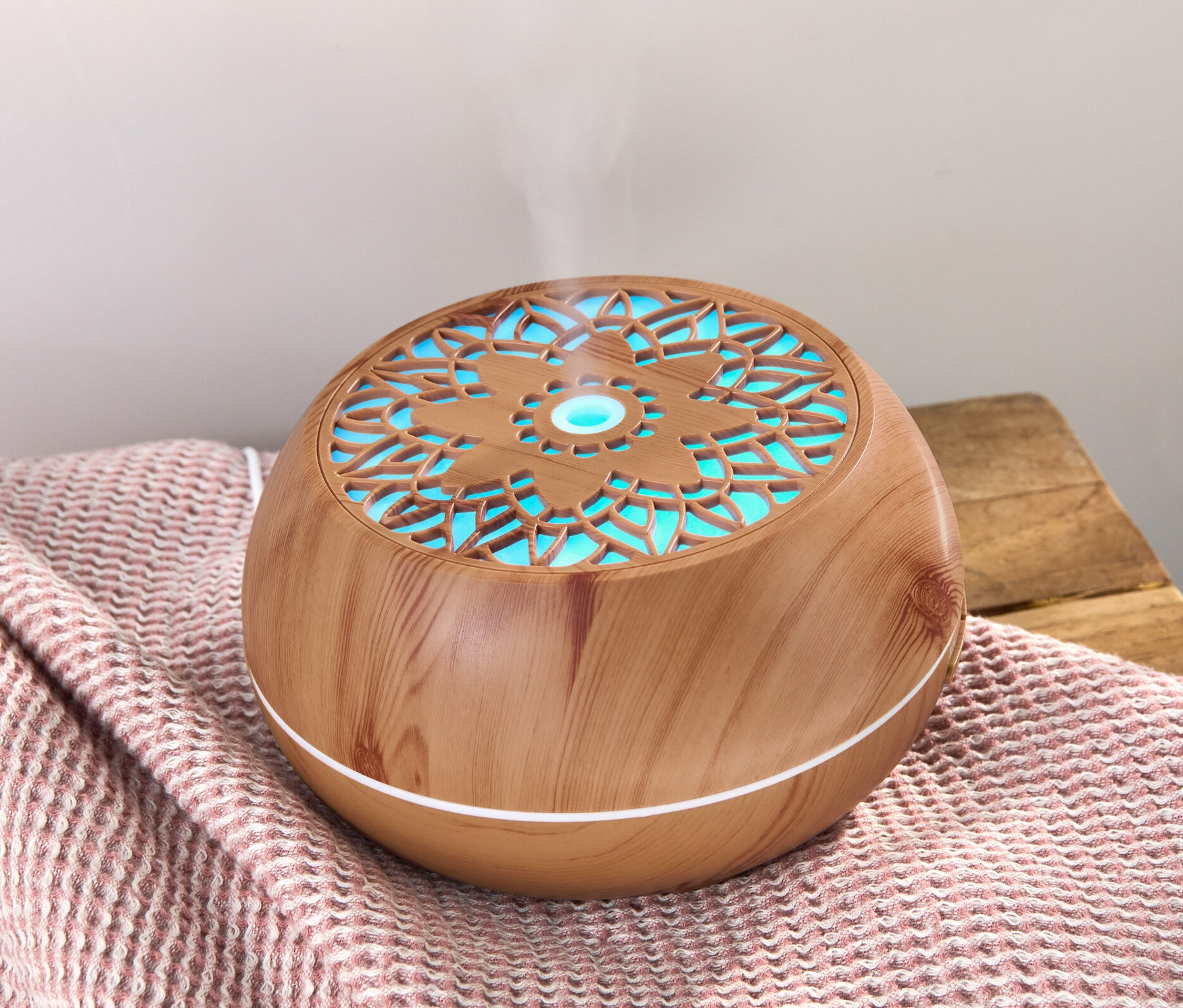 Aroma diffúzor Bluetooth® hangszóróval egy rózsaszín takarón, amiből gőz száll fel.