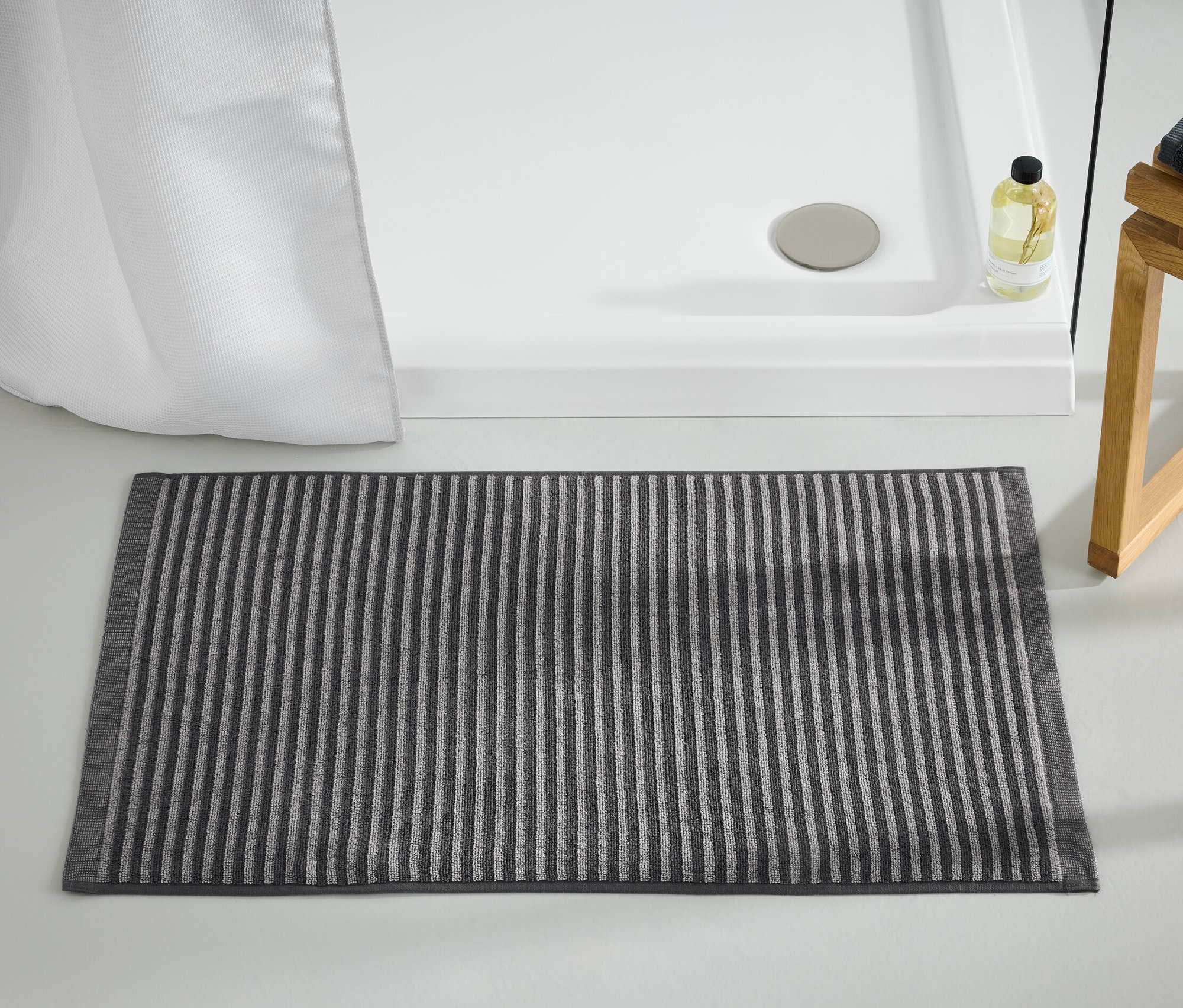 Antracit színű, csíkos fürdőszobaszőnyeg a zuhanykabin mellett.