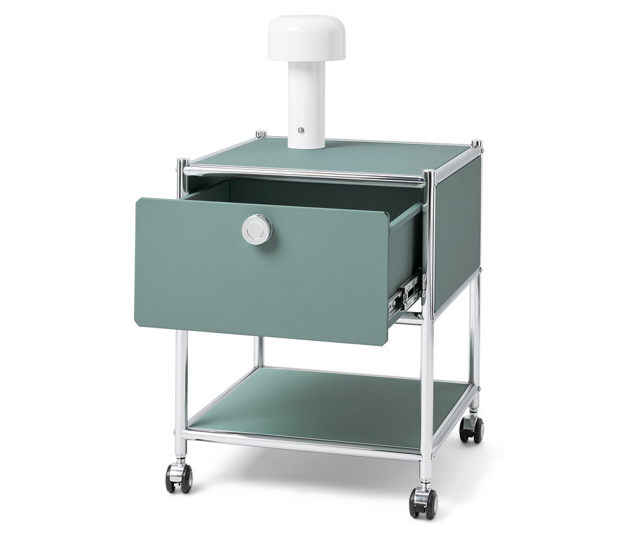 Zöld éjjeliszekrény nyitott fiókkal és fehér lámpával a tetején.