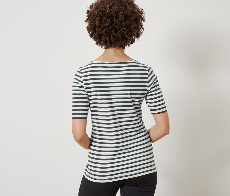 Hátulról látható egy barna, göndör hajú nő, aki egy zöld csíkos, félhosszú ujjú felsőt és egy fekete nadrágot visel.