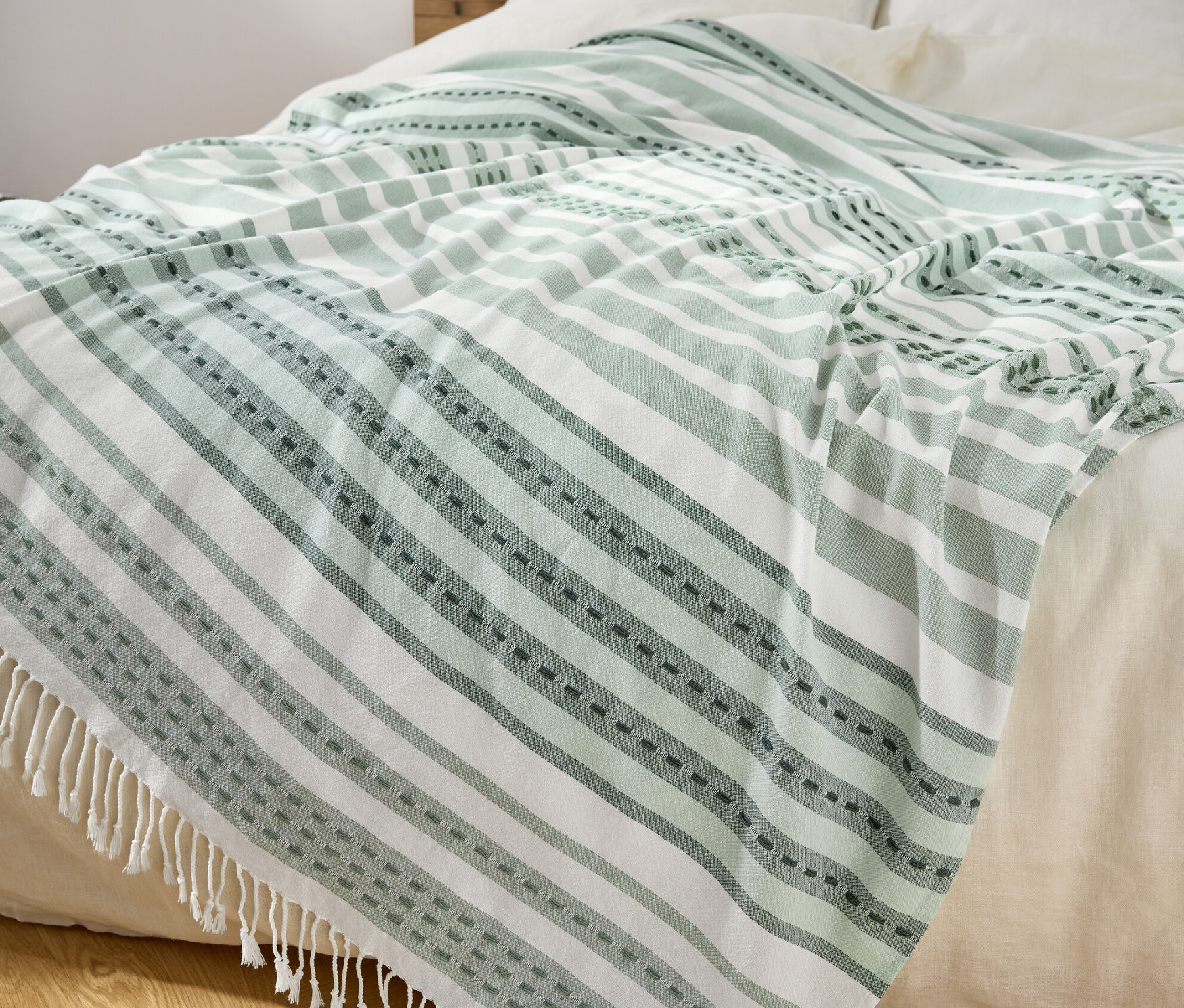 Egy ágyon zöld és fehér csíkos, rojtokkal ellátott pléd fekszik.