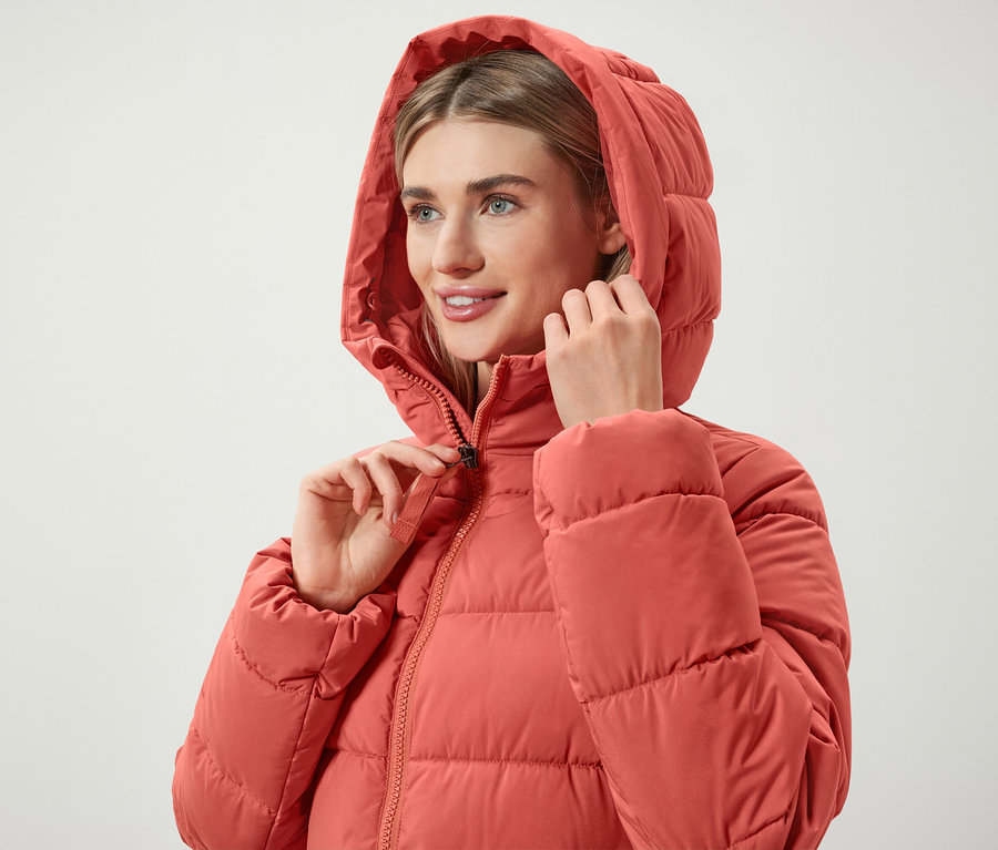 Nő cipzározza a korallpiros, kapucnis pehelykabátját.