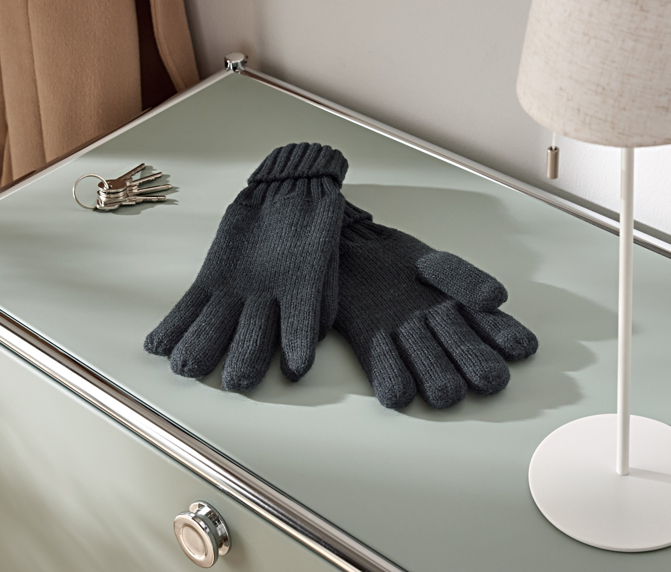 A szekrényen egy pár kötött kesztyű, egy kulcscsomó és egy lámpa van.